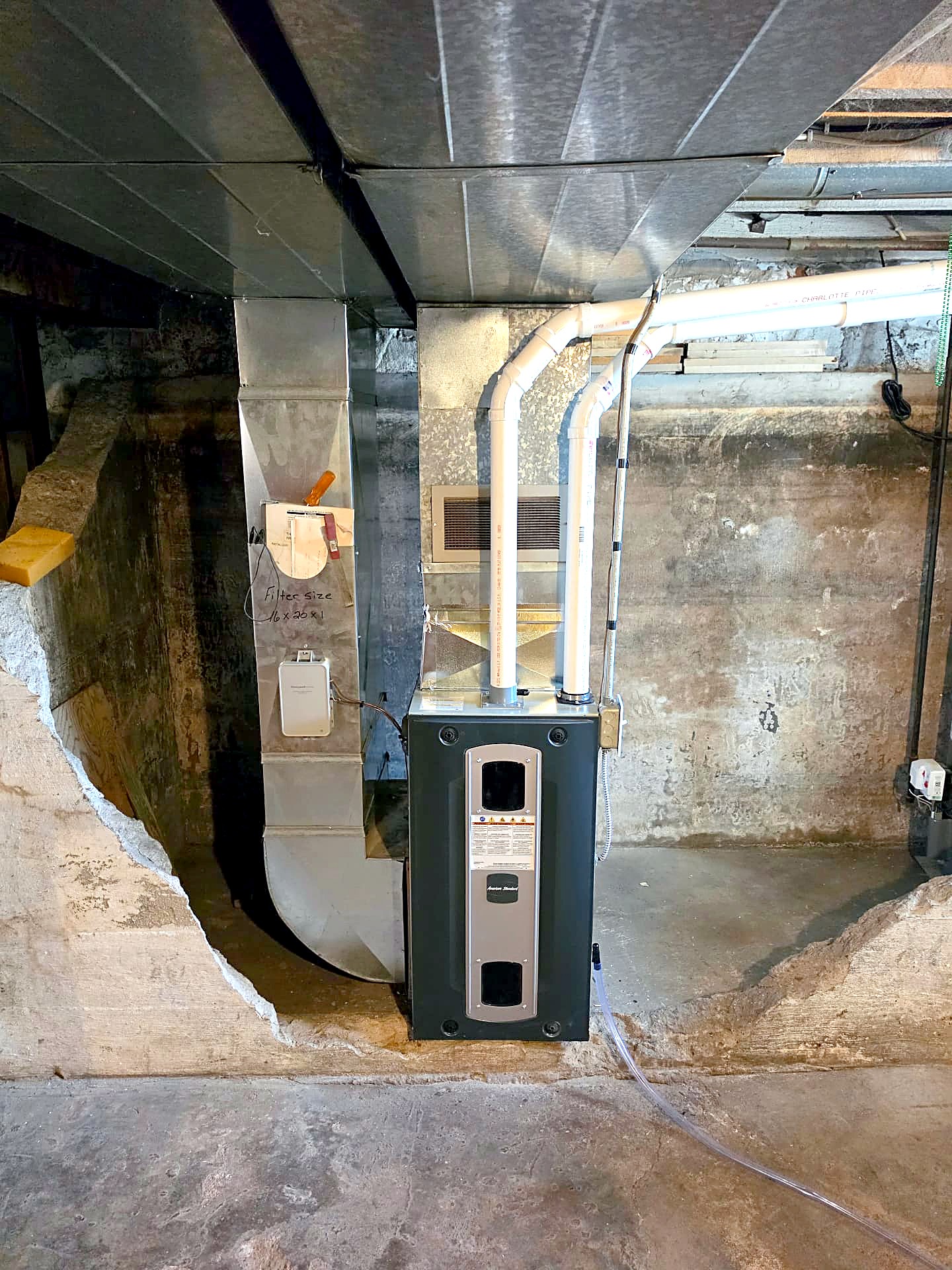 American Standard furnace set into a basement wall with supply duct and vent piping
